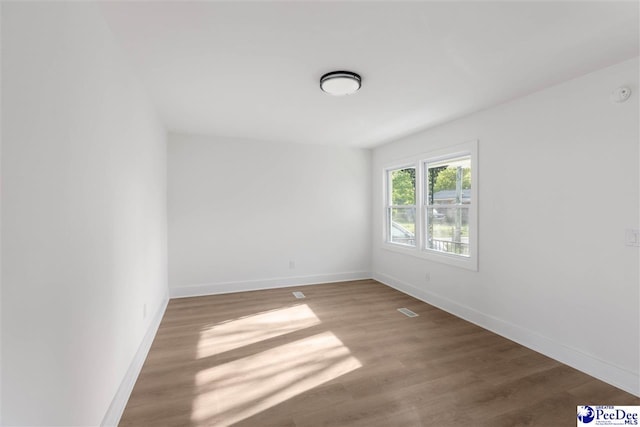 unfurnished room with visible vents, baseboards, and wood finished floors