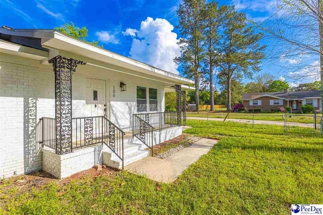 doorway to property with brick siding, a yard, a porch, and fence