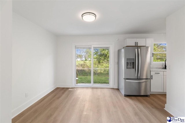 kitchen with light wood finished floors, baseboards, stainless steel fridge, and white cabinets