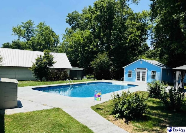 outdoor pool with a patio, a storage structure, french doors, and an outbuilding