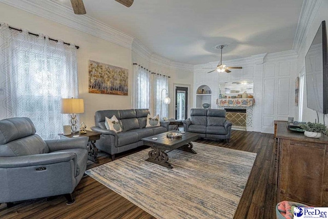 living area featuring dark wood-style flooring, ceiling fan, a stone fireplace, and crown molding