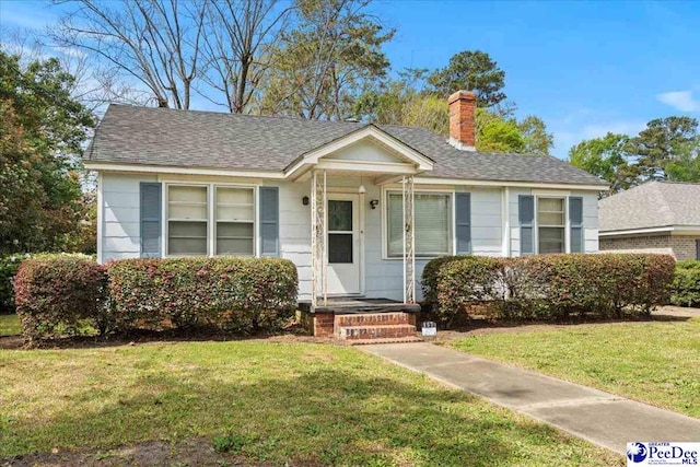 bungalow-style home with a chimney, a shingled roof, and a front lawn