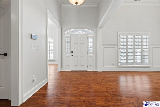 foyer featuring a towering ceiling, dark wood finished floors, crown molding, and a decorative wall