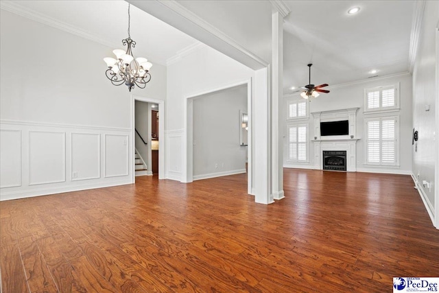 unfurnished living room featuring ornamental molding, ceiling fan with notable chandelier, dark wood-style floors, a fireplace, and a decorative wall