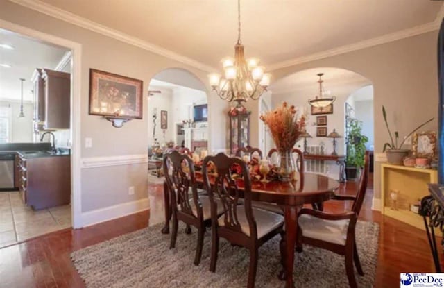 3438 Hammock Ct, Florence, SC 29501 - dining room featuring light wood finished floors, arched walkways, a notable chandelier, and crown molding