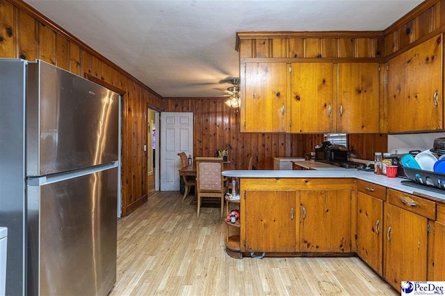 kitchen with wood walls, light wood-type flooring, stainless steel fridge, kitchen peninsula, and ceiling fan