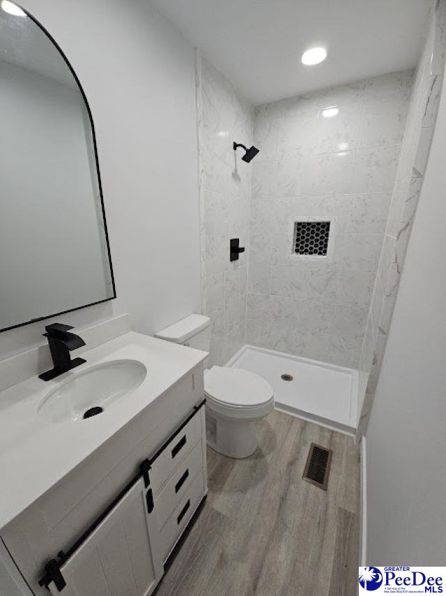 bathroom with vanity, a tile shower, hardwood / wood-style floors, and toilet