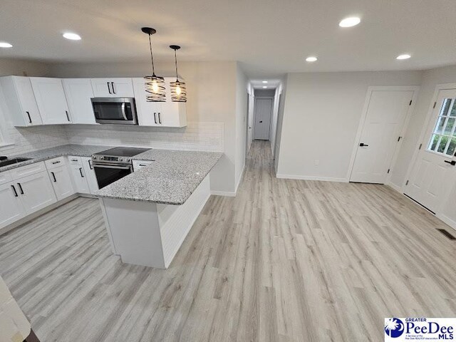 kitchen with appliances with stainless steel finishes, white cabinets, hanging light fixtures, kitchen peninsula, and light stone countertops