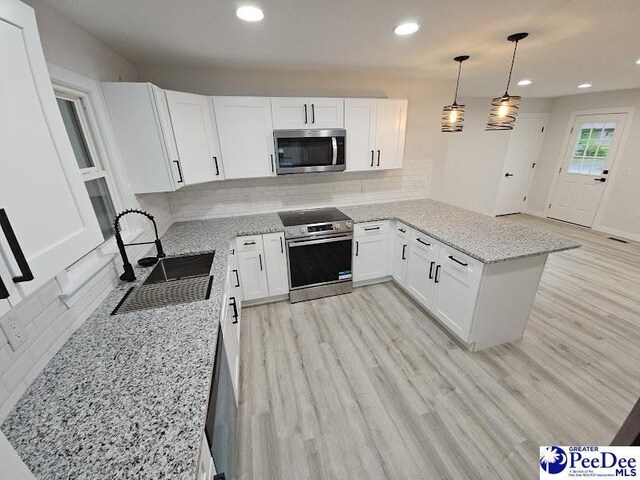 kitchen featuring appliances with stainless steel finishes, pendant lighting, white cabinetry, sink, and kitchen peninsula