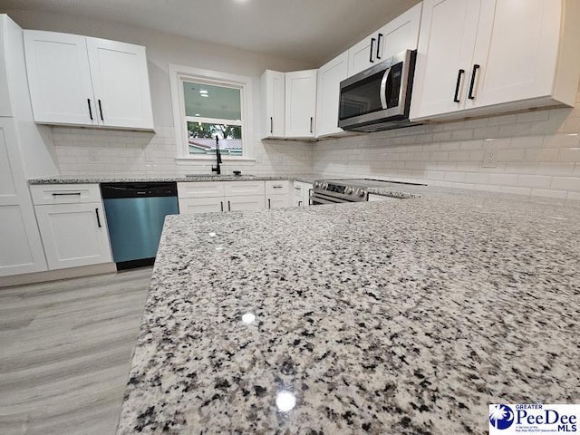 kitchen with white cabinetry, sink, light stone countertops, and appliances with stainless steel finishes