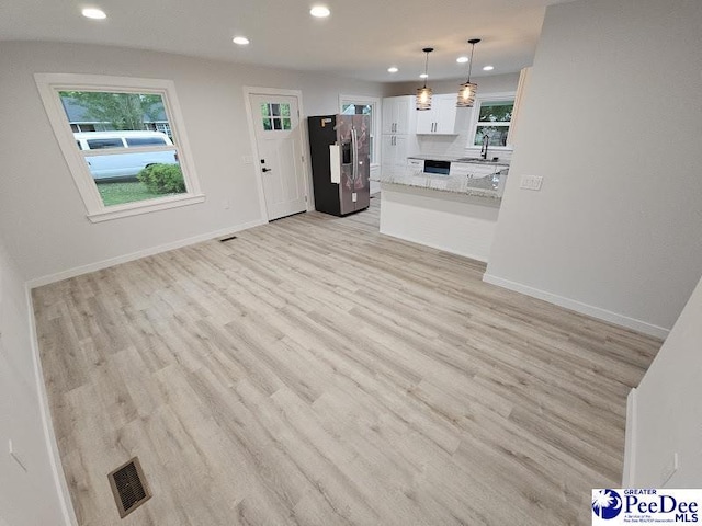 kitchen featuring pendant lighting, white cabinetry, light stone counters, stainless steel fridge with ice dispenser, and light hardwood / wood-style flooring