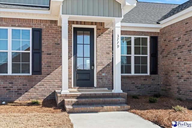 doorway to property with brick siding, roof with shingles, and board and batten siding