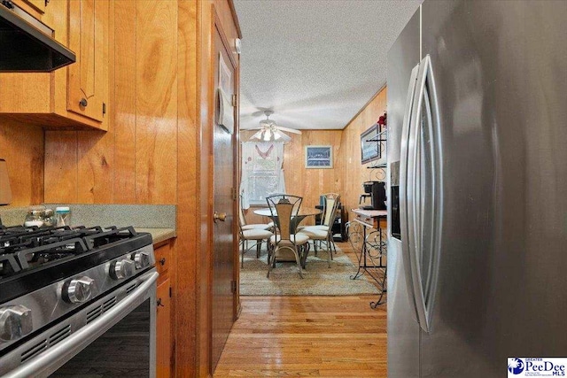 kitchen featuring a textured ceiling, under cabinet range hood, a ceiling fan, appliances with stainless steel finishes, and light wood-type flooring