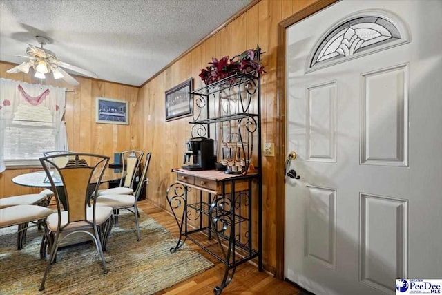 dining space with a ceiling fan, ornamental molding, a textured ceiling, wooden walls, and wood finished floors