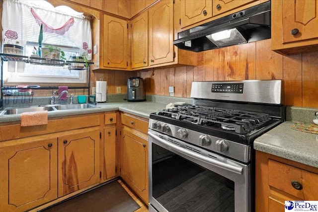 kitchen featuring stainless steel gas range oven, under cabinet range hood, a sink, light countertops, and brown cabinetry