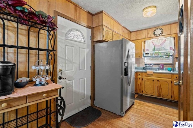 kitchen featuring wooden walls, crown molding, light wood-style flooring, and stainless steel refrigerator with ice dispenser