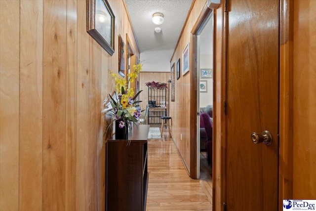 hall with a textured ceiling, light wood finished floors, and wooden walls