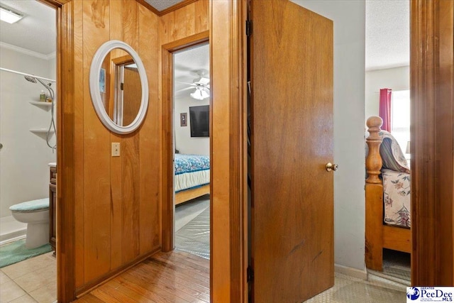 hallway featuring a textured ceiling, light wood-style flooring, wood walls, baseboards, and ornamental molding