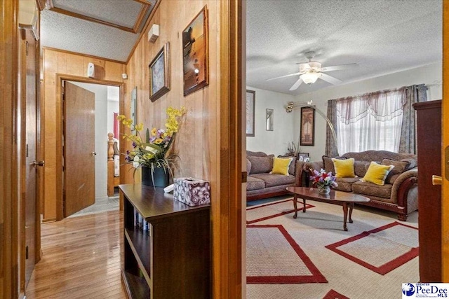 living room featuring a textured ceiling, wood walls, light wood-style flooring, and a ceiling fan