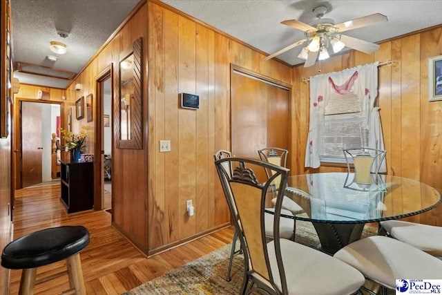 dining area featuring a textured ceiling, wood walls, light wood-type flooring, and a ceiling fan