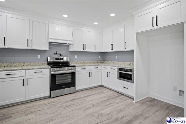 kitchen featuring premium range hood, white cabinets, stainless steel appliances, light stone countertops, and light hardwood / wood-style flooring