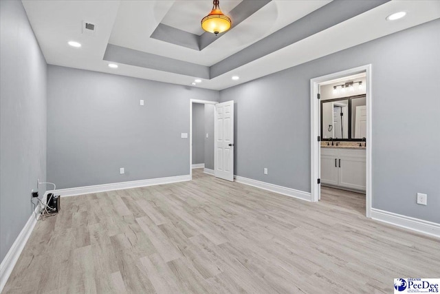 unfurnished bedroom with connected bathroom, light hardwood / wood-style flooring, and a tray ceiling