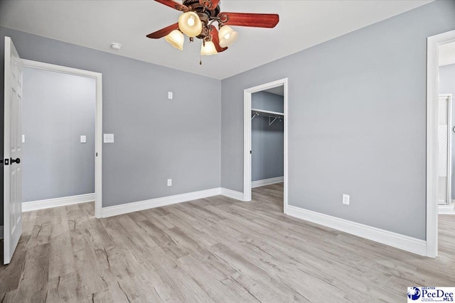 unfurnished bedroom featuring ceiling fan, a closet, a spacious closet, and light hardwood / wood-style flooring