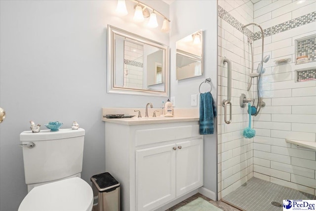bathroom with a tile shower, toilet, and vanity