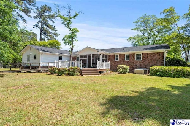 rear view of house featuring a lawn, a sunroom, brick siding, and a deck