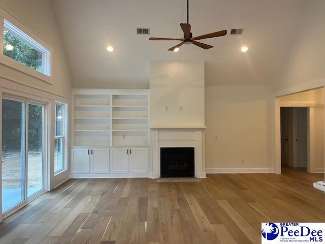 unfurnished living room featuring built in shelves, ceiling fan, high vaulted ceiling, and light wood-type flooring