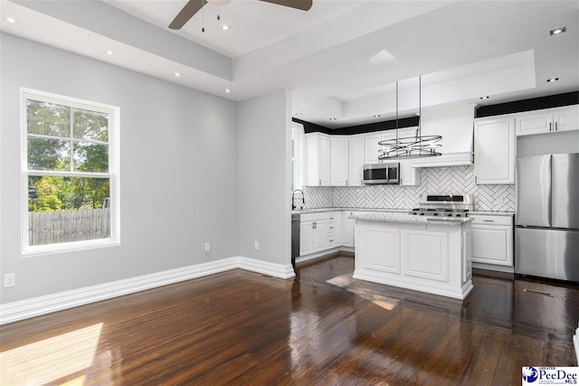 kitchen featuring stainless steel appliances, tasteful backsplash, white cabinets, decorative light fixtures, and a raised ceiling