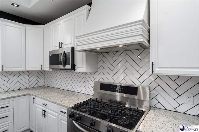 kitchen featuring premium range hood, appliances with stainless steel finishes, white cabinetry, backsplash, and light stone counters