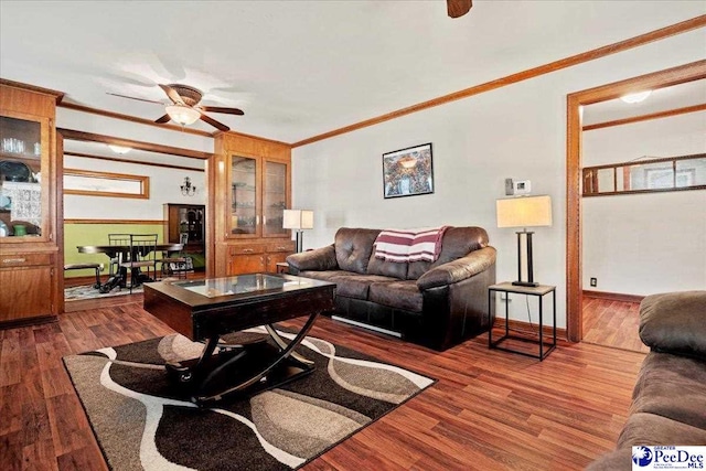 living room with baseboards, crown molding, a ceiling fan, and wood finished floors