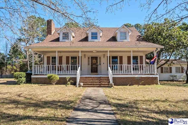 view of front of house featuring covered porch, a front lawn, and a chimney