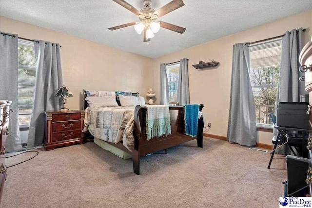 carpeted bedroom featuring a textured ceiling, multiple windows, a ceiling fan, and baseboards