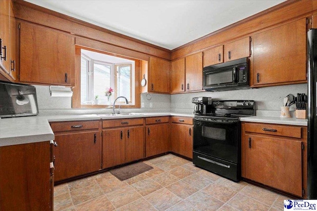 kitchen with black appliances, brown cabinets, a sink, and light countertops