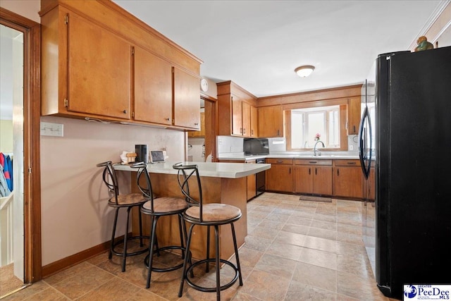 kitchen featuring light countertops, brown cabinetry, freestanding refrigerator, a peninsula, and baseboards