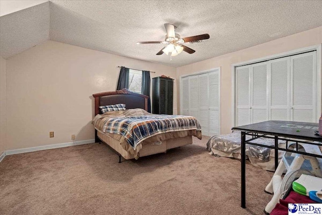 bedroom featuring baseboards, a ceiling fan, light colored carpet, a textured ceiling, and multiple closets