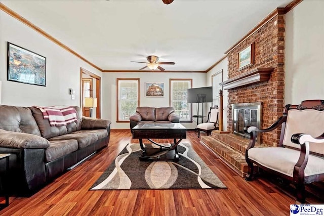 living room featuring a ceiling fan, a brick fireplace, crown molding, and wood finished floors