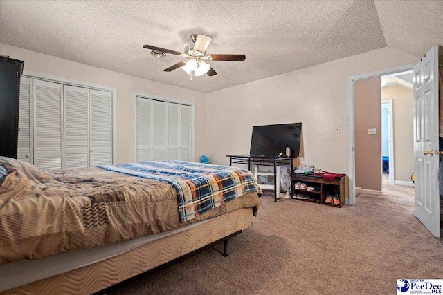 bedroom with baseboards, ceiling fan, a textured ceiling, carpet floors, and two closets