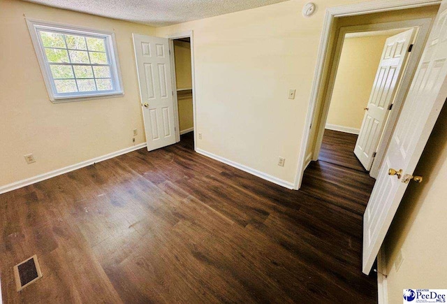 unfurnished bedroom featuring dark wood-style flooring, visible vents, baseboards, and a textured ceiling