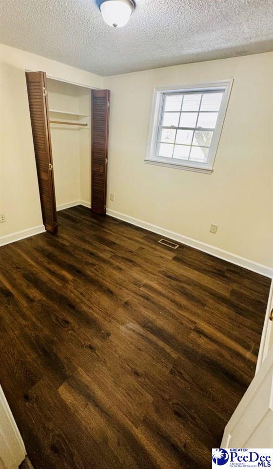 unfurnished bedroom featuring a closet, baseboards, dark wood-style floors, a textured ceiling, and visible vents