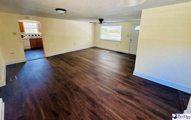 unfurnished living room featuring a wealth of natural light, visible vents, dark wood-style flooring, and a ceiling fan