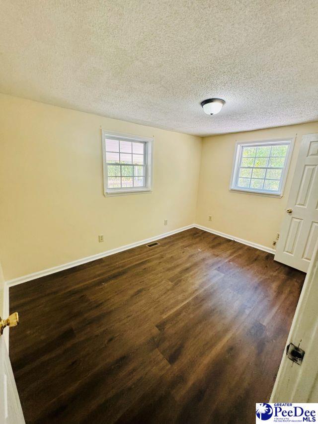 empty room with a textured ceiling, dark wood-style flooring, baseboards, and visible vents