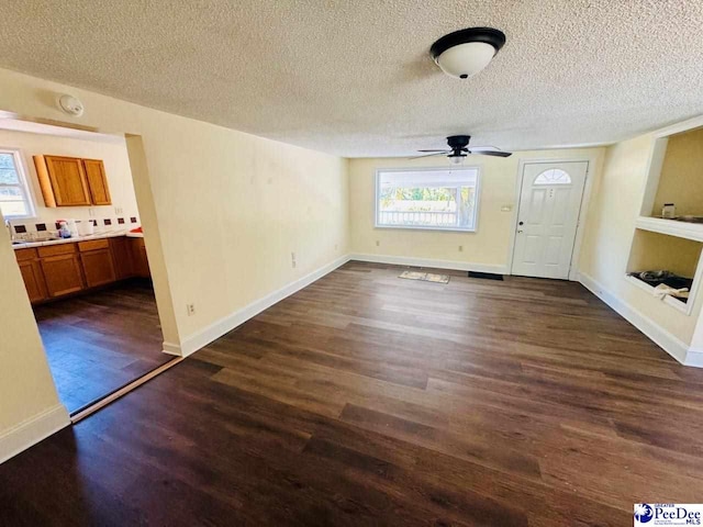 unfurnished living room with dark wood-type flooring, a textured ceiling, baseboards, and a ceiling fan