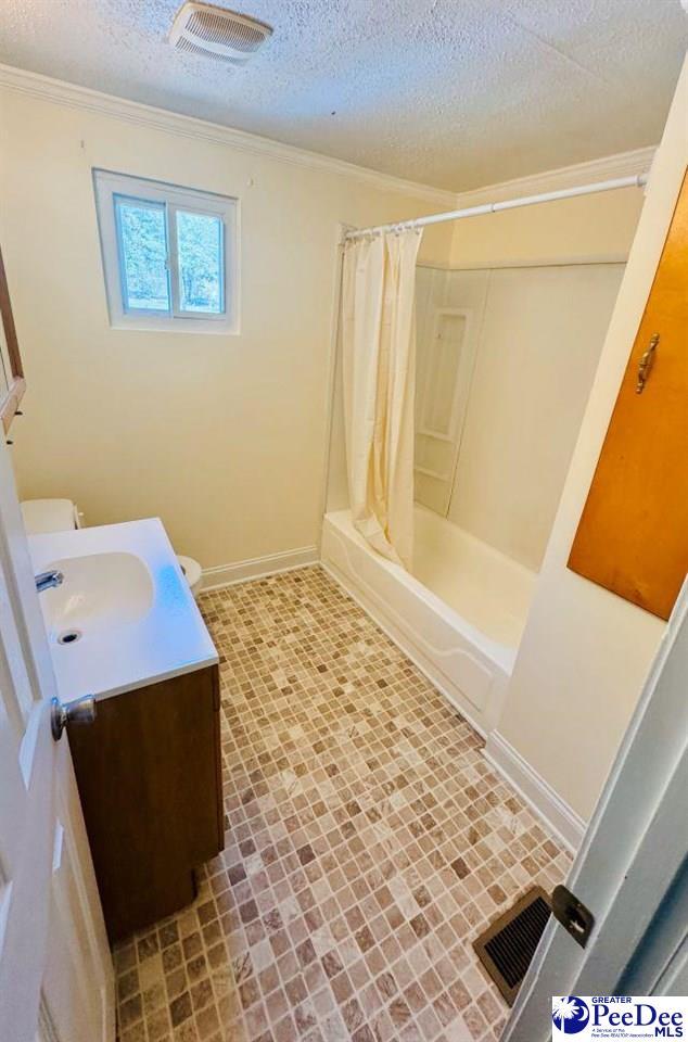 full bath featuring vanity, baseboards, a textured ceiling, crown molding, and visible vents