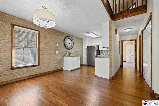 kitchen with a sink, freestanding refrigerator, a textured ceiling, dark wood finished floors, and white cabinets
