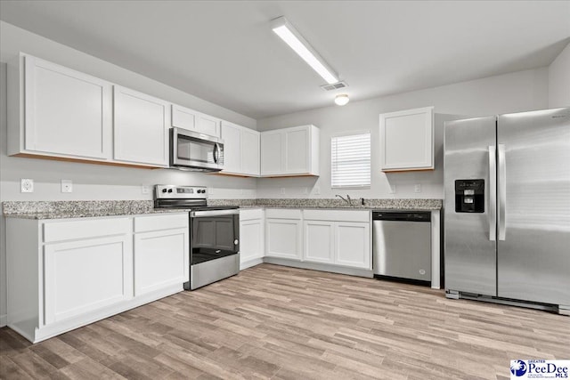3229 Winding Way Dr, Florence, SC 29506 - kitchen featuring appliances with stainless steel finishes, white cabinets, light wood-type flooring, and light stone counters