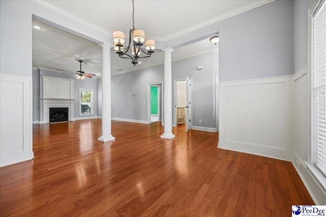 unfurnished living room with crown molding, ceiling fan with notable chandelier, wood-type flooring, and decorative columns