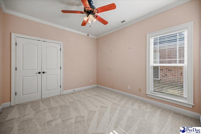 unfurnished bedroom with ornamental molding, light colored carpet, ceiling fan, and a closet